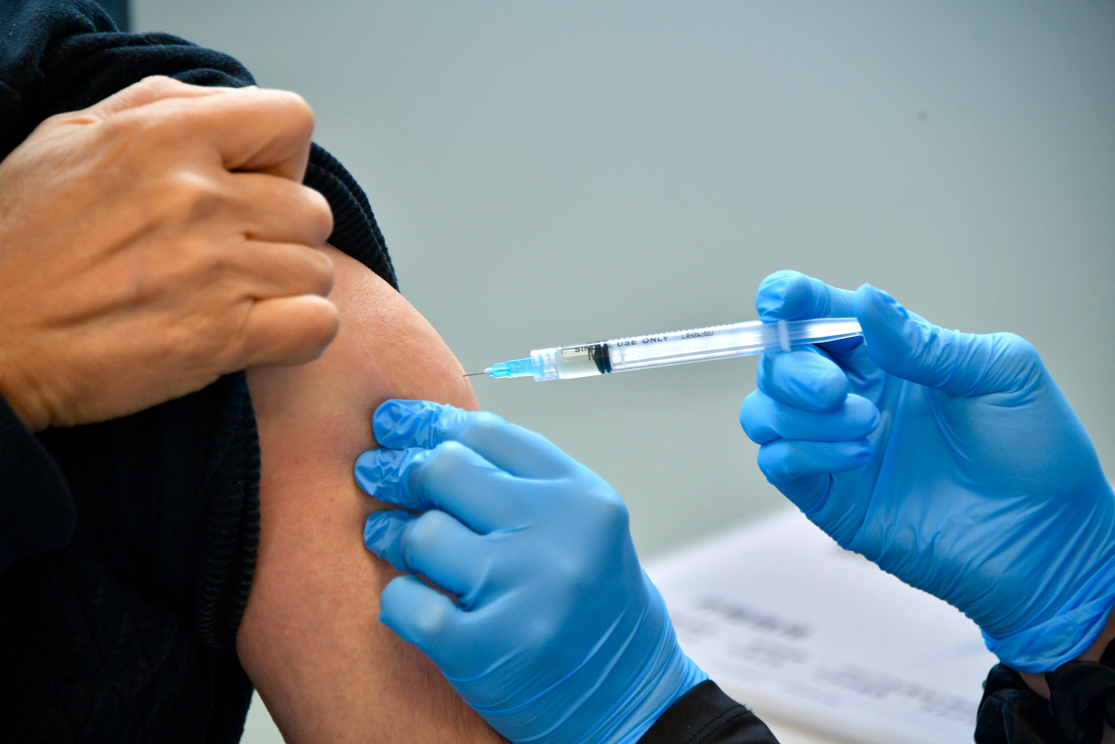 A nurse in blue gloves administering an injection to a patient's arm
